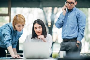 three people hover over a laptop